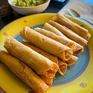 Mexican chicken Flautas taquitos on yellow plate with guacamole in the background for dinner.