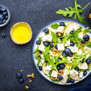 Tasty salad with pears, blueberries, roquefort cheese, arugula and nuts. Black background, top view