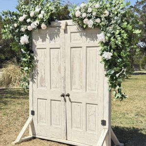Rustic white vintage aisle doors with lush greenery and white floral garland wedding ceremony backdrop