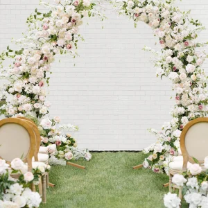 Elegant curved floral wedding arch decorated with white and blush roses and greenery, ceremony setup with chairs