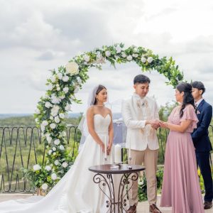 Bride and groom exchanging vows beneath a white floral wedding arch with lush greenery during an outdoor ceremony overlooking the Texas Hill Country.