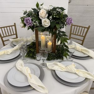 Rustic wooden lantern centerpiece with pillar candles, greenery, and artificial lavender and white roses